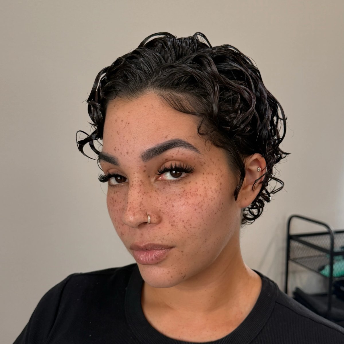Woman with freckles sporting a sleek wet-look dark curly pixie cut