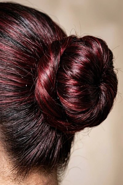 Close-up of a twisted high bun showing dark brunette roots and glossy cherry red highlights