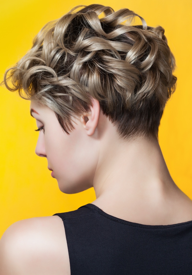 Rear three-quarter view of a blonde wavy pixie cut with a closely cropped nape undercut