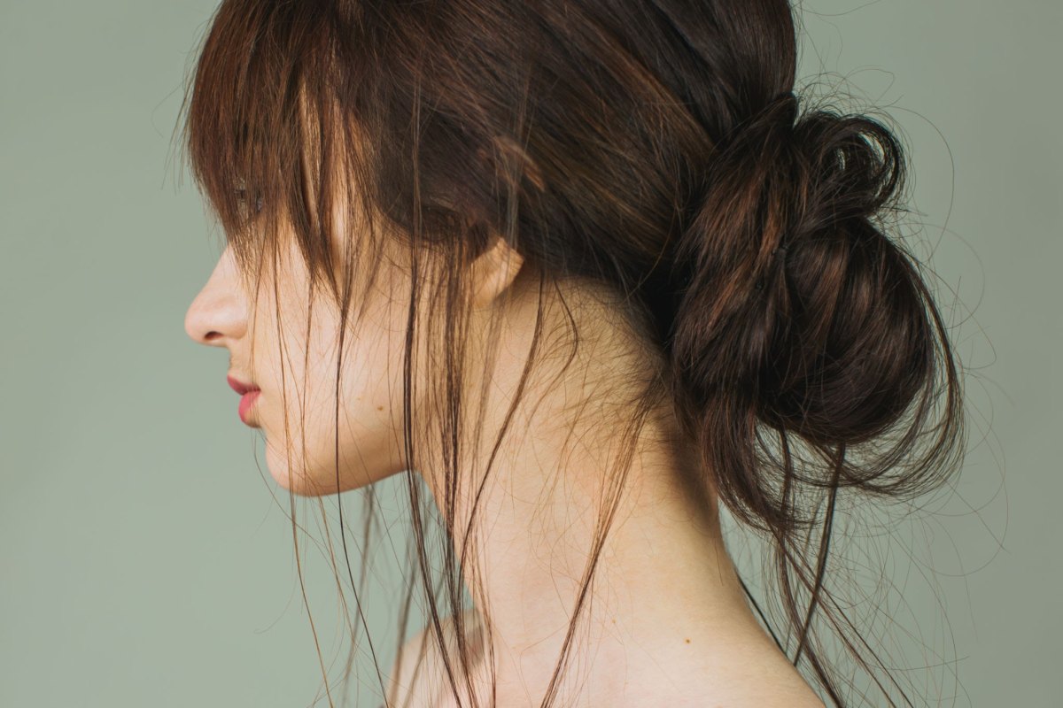 Side profile of a messy bun updo with long wispy bangs and neck tendrils