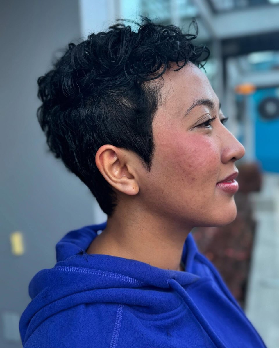 Profile of a person in a blue hoodie with a natural dark tousled short curly pixie cut