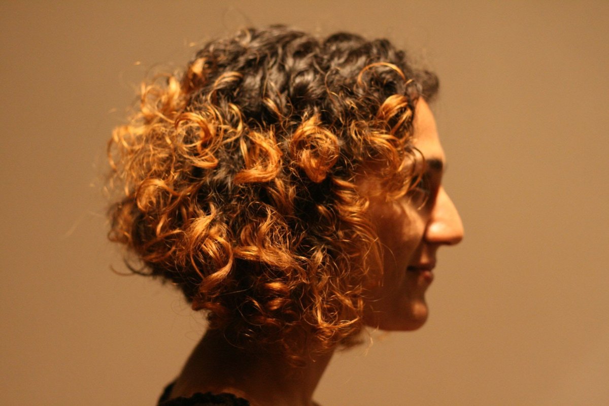 Profile shot of a curly crop with dark roots and warm copper highlights