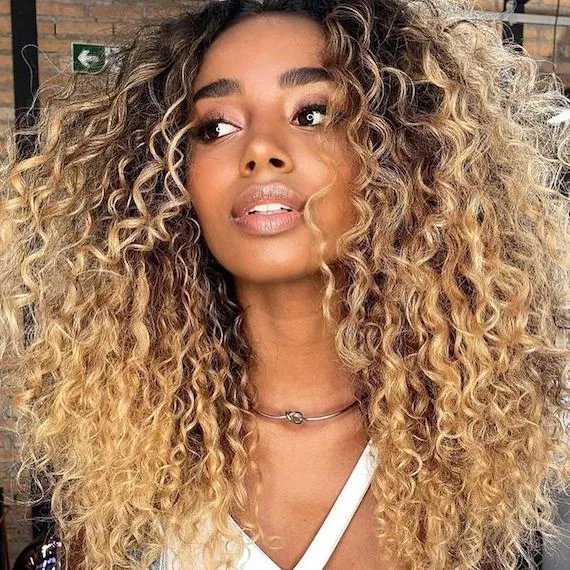 Voluminous curly hair with dark roots and honey blonde balayage